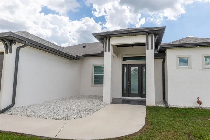 Welcome home! The striking front entrance of this modern Punta Gorda custom home features an elegant concrete walkway, crisp white stucco exterior, high architectural arches, and contemporary dark trim accents. Exceptional curb appeal sets the stage for luxury Florida living.