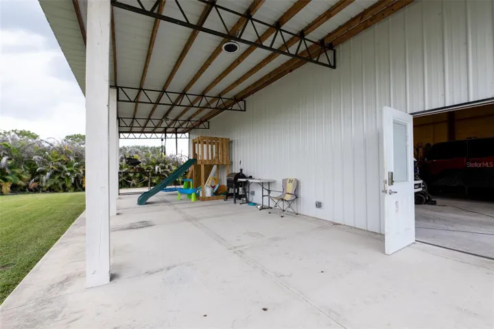 A closer look at the expansive concrete pad underneath the detached building’s massive covered overhang. This versatile space provides excellent shade and endless options for outdoor entertaining, working on projects, or additional vehicle parking.