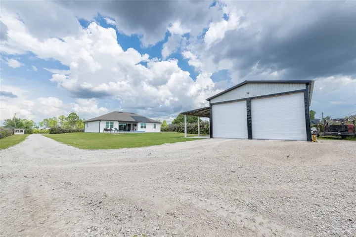 Comprehensive property overview showing the expansive gravel driveway, massive detached workshop garage, and the main pool residence in the distance. An exceptional find for buyers seeking land, premium storage, and a modern custom home with no HOA restrictions.