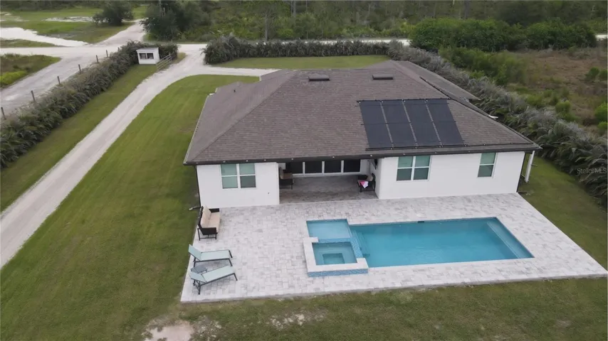 Spectacular bird's-eye aerial view capturing the ultimate backyard paradise. This premium acreage property features a massive brick paver sun deck, a custom geometric swimming pool with an integrated raised spa, a deep shaded lanai footprint, and a high-efficiency rooftop solar panel system to keep your utility costs incredibly low.