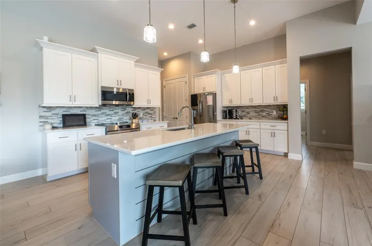 A chef's dream! This gourmet kitchen boasts a massive central island with stylish shiplap detailing and breakfast bar seating, pristine quartz countertops, timeless white shaker cabinets, premium stainless steel appliances, and elegant glass pendant lighting.