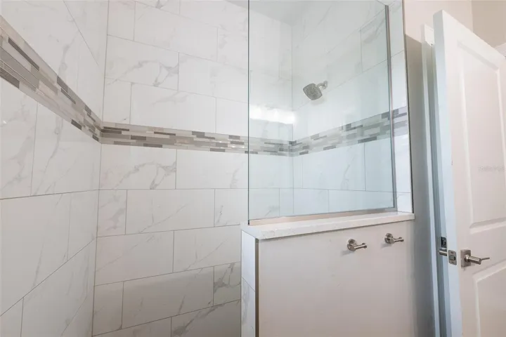 Indulge in the luxury walk-in guest shower, meticulously detailed with high-end marble-look porcelain tile, a contemporary multi-tonal mosaic accent band, an undermount shower pan, and a custom glass splash partition wall.