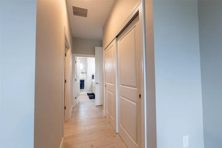This wide hallway view highlights the desirable split floor plan layout, connecting the primary retreat to the main living spaces. Features include solid-core interior doors, uniform tile flooring, and large storage closets.