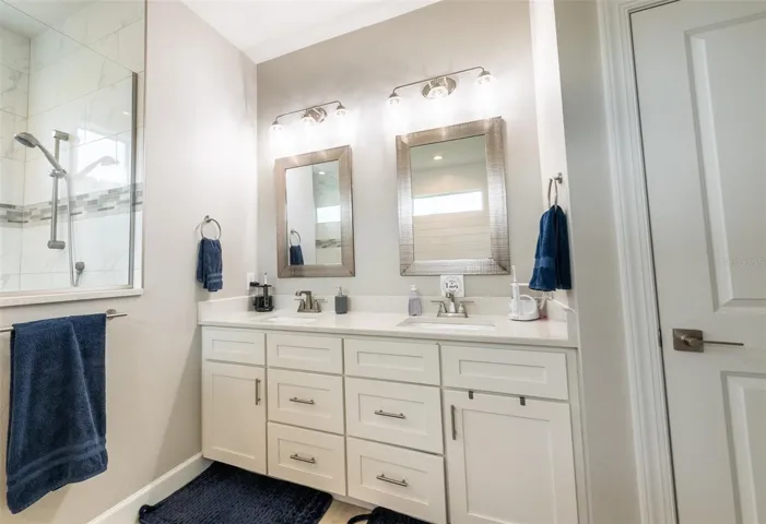 The primary bathroom's oversized double vanity features timeless white shaker cabinetry, an abundance of storage drawers, elegant quartz countertops, dual undermount sinks, and contemporary brushed metal hardware beneath transitional vanity lighting.