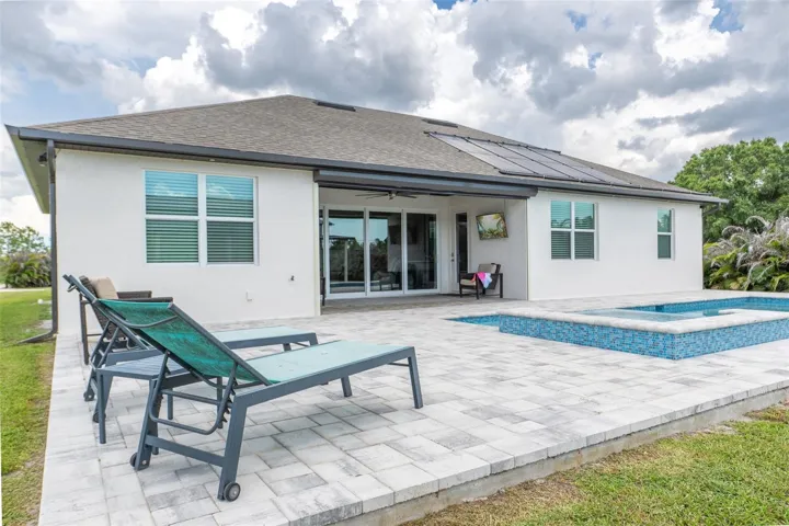 Step into your private backyard oasis. The rear exterior boasts a pristine custom swimming pool and spa lined with vibrant blue tile, an expansive paver patio deck for sunloungers, and energy-efficient solar panels on the roof to keep utility costs low.