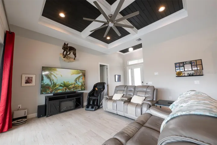 The spacious great room defines modern luxury with its soaring custom tray ceiling, contrasting dark wood shiplap accent, and a massive industrial ceiling fan. The bright, open-concept living area flows effortlessly, making it the perfect central gathering space.