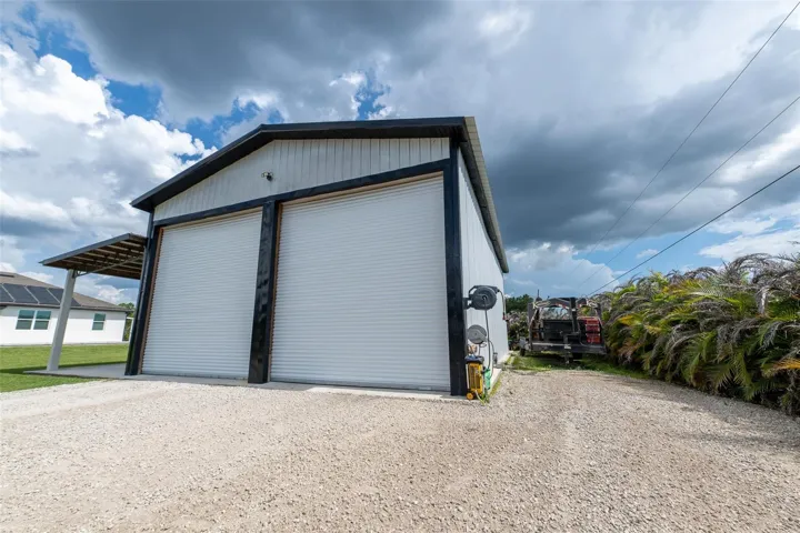 Heavy-duty exterior view of the detached workshop’s commercial-grade, dual roll-up garage doors. Designed for easy drive-in access for oversized trucks, RVs, or boats, with a wide gravel driveway offering plenty of heavy equipment turnaround space.