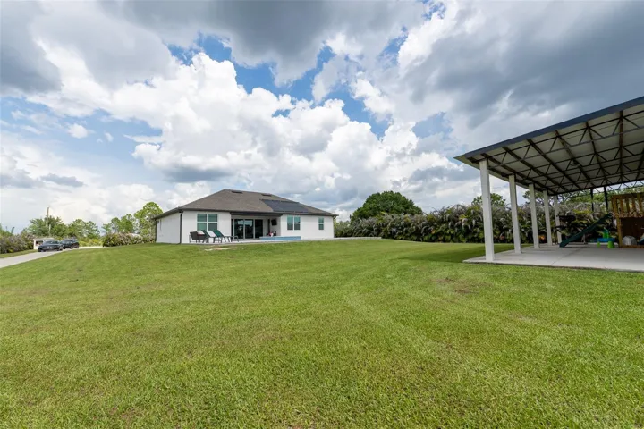 Sprawling wide-angle view of the massive backyard lawn separating the primary residence and the massive outbuilding. This premium acreage lot offers limitless potential for additional landscaping, gardening, or a secure compound setup.