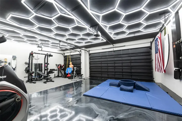 Showstopper alert! This angle of the ultra-custom garage gym highlights the spectacular high-gloss black and silver metallic epoxy floor coating, offering a mirror-like finish. This incredible, conditioned space easily doubles back into a premium vehicle showroom or a dream workshop.