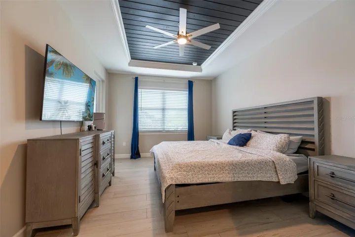 Alternate view of the spacious primary suite demonstrates ample room for full-sized king furniture, dressers, and nightstands. The uniform wood-look porcelain tile flooring adds a touch of modern warmth to this bright and airy bedroom.