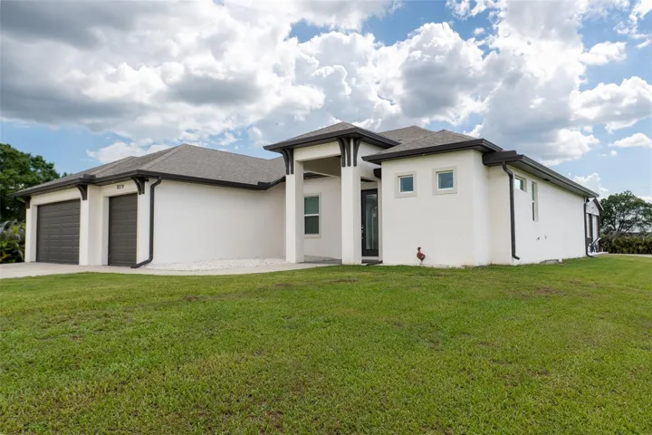 Grand exterior view showcasing the expansive front elevation and attached multi-car garage. Situated on a sprawling, beautifully manicured green lot, this property offers incredible privacy and premium construction with impact-resistant windows and low-maintenance landscaping.