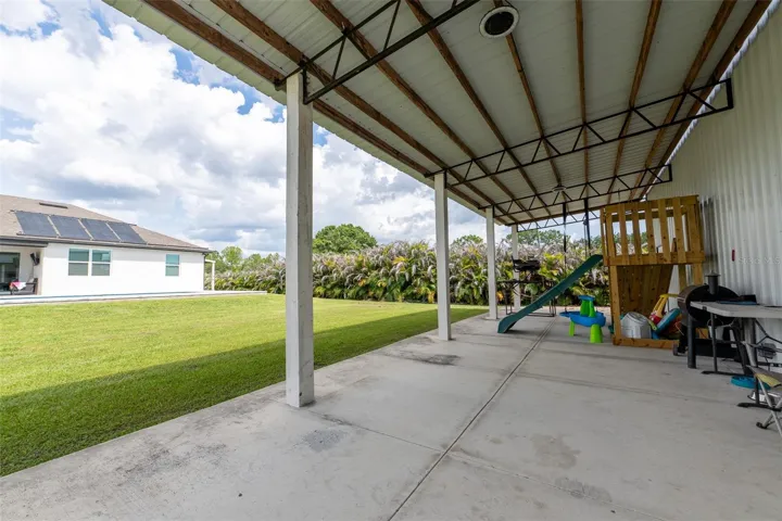 View looking out from the detached workshop across the vast, open green acreage toward the main pool home. Enjoy wide-open spaces, a secure perimeter with privacy hedges, and the absolute best of indoor-outdoor country-style living.