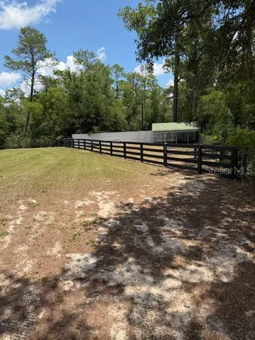 back left corner of property with wood fenced in horse turnout with metal shed for shade