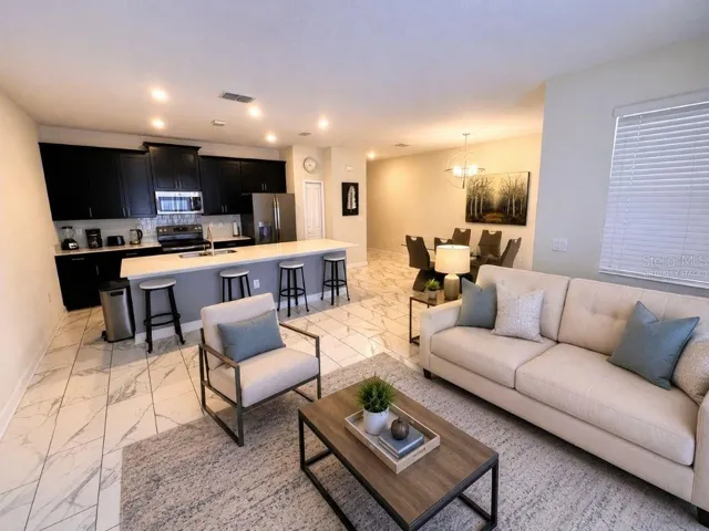 Virtually staged open-concept living area highlighting the large kitchen island, dining space, and comfortable layout for everyday living or vacation guests.