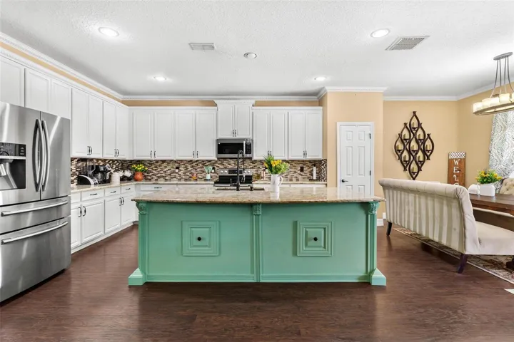 Kitchen features stainless steel appliances, granite countertops, stylish backsplash, cooper sink, and large center island while overlooking dinette and family room.