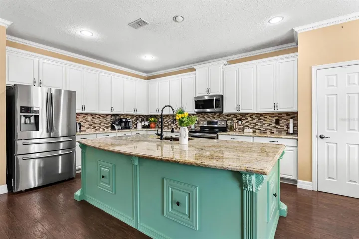 Kitchen features stainless steel appliances, granite countertops, stylish backsplash, cooper sink, and large center island while overlooking dinette and family room.
