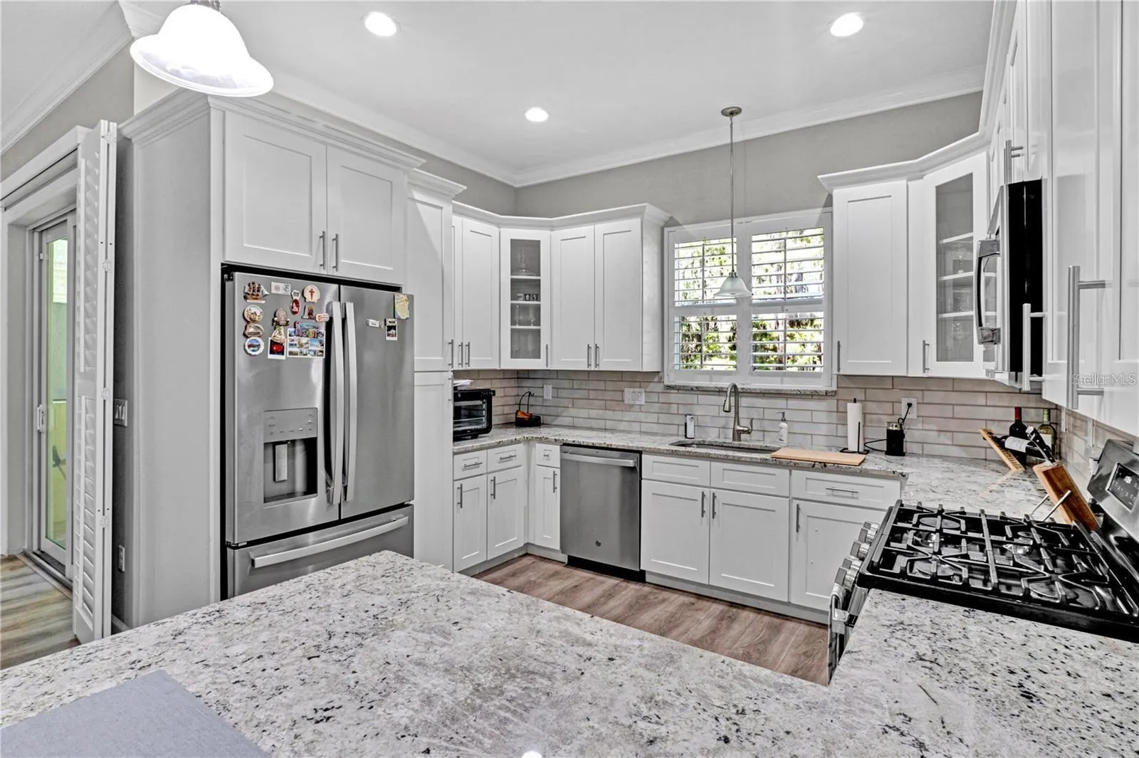 This chef-inspired kitchen features gleaming granite countertops, bright white shaker cabinets, stainless steel appliances, and a massive breakfast bar island.