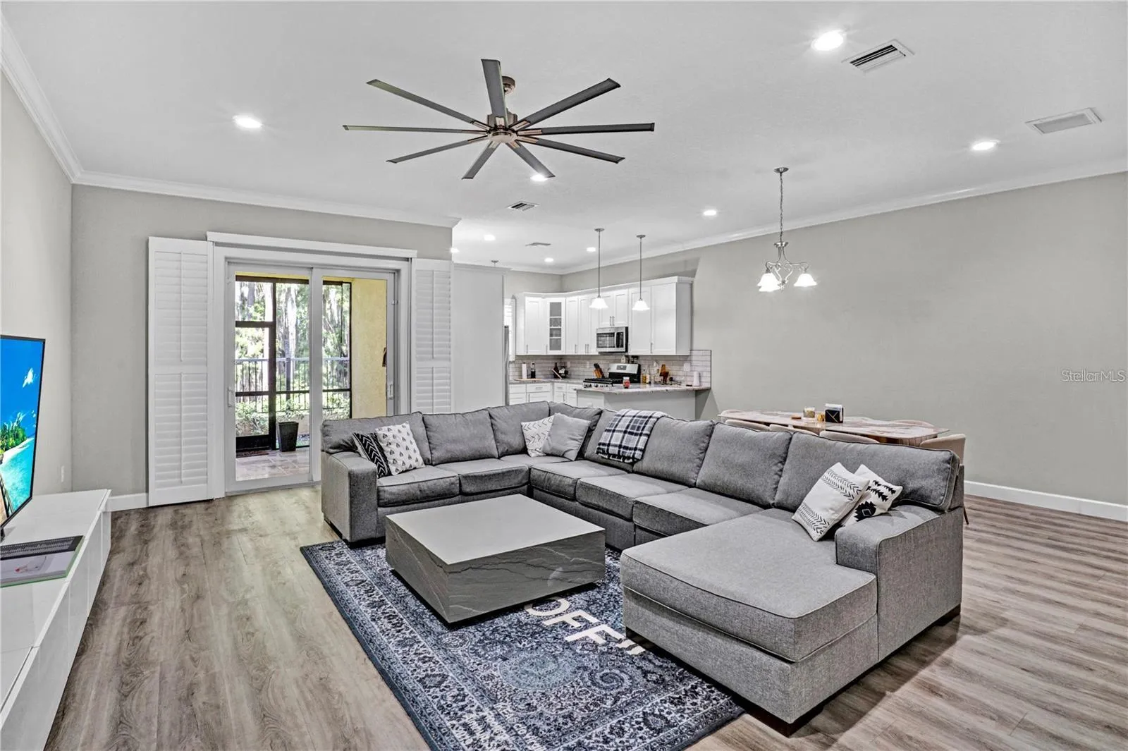 A view of the generous living room layout, showcasing a vast accent wall ideal for a large entertainment center, flanked by elegant plantation shutters.