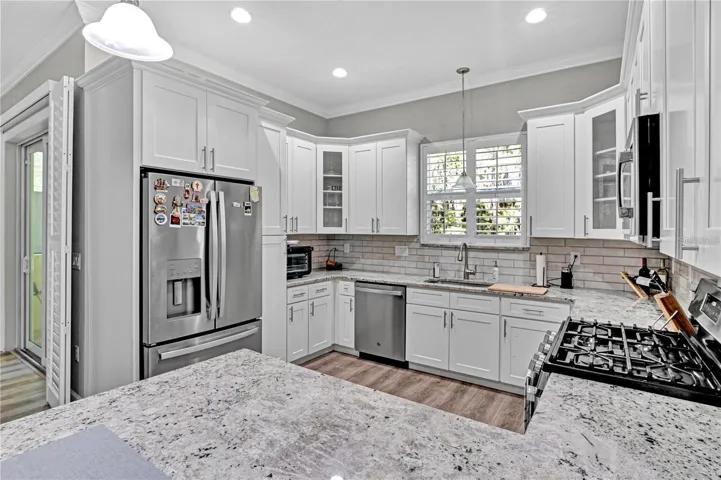 This chef-inspired kitchen features gleaming granite countertops, bright white shaker cabinets, stainless steel appliances, and a massive breakfast bar island.