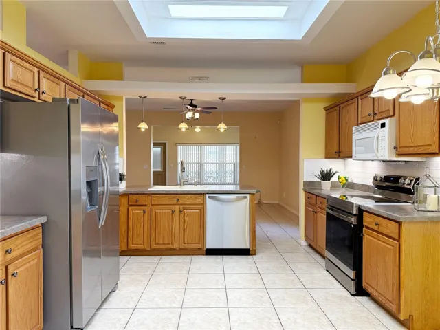 Kitchen with solid wood cabinets, ceramic tile flooring, tile backsplash, under cabinet lighting, stainless steel appliances, closet pantry, bar top seating with pendant lighting, decorative shelf and open to the Dining and Family rooms