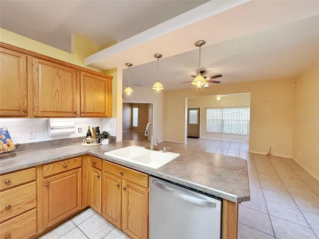 Kitchen with view of Family and Florida room and double door entry to Primary bedroom, tile backsplash, solid wood cabinets with under cabinet lighting, bar top seat with pendant lighting