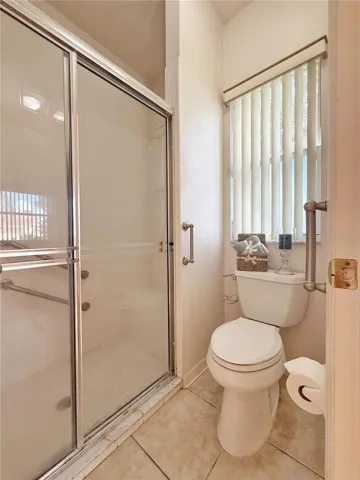 Primary bathroom water closet and shower with glass door, ceramic tile flooring