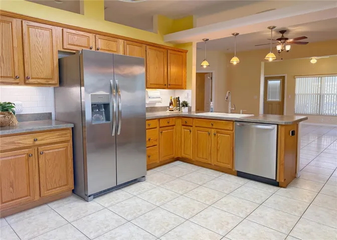 Kitchen with ceramic tile flooring, stainless steel appliances, bar top seating with pendant lighting, solid wood cabinets with under lighting, tile backsplash, pantry