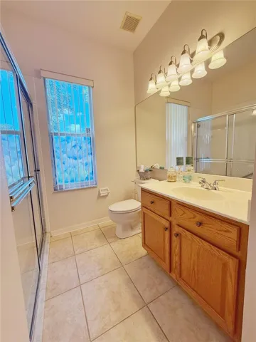 Bathroom 2 with tub/shower combo with glass door, solid wood cabinet, ceramic tile flooring, linen closet