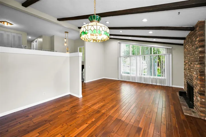Large living and dining room area with gleaming wood floors and beamed, vaulted ceiling.