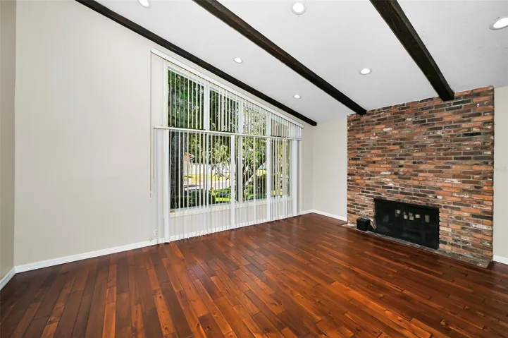 A warm, inviting living room with a vaulted beamed ceiling, a large centerpiece fireplace, and rich hardwood floors.