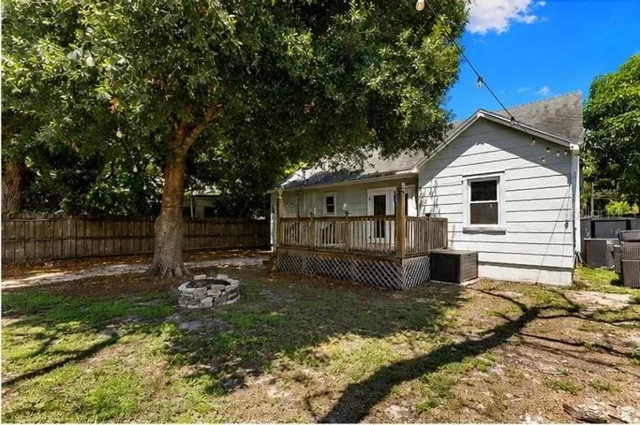IGenerous fenced backyard with a cozy stone fire pit and towering shade trees — room to garden, gather, or unwind.