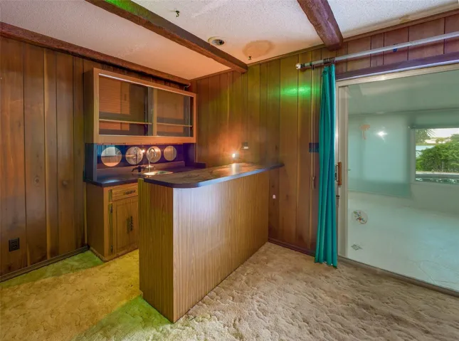 Built in wet bar with sink, glass front cabinetry, and exposed beams