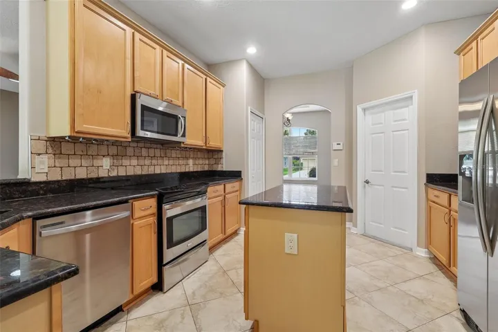 The beautifully UPDATED Kitchen is a true showpiece, featuring abundant cabinetry, granite countertops, NEW TRAVERTINE TILE BACKSPLASH, stainless steel appliances, a kitchen island, breakfast bar, closet pantry, and NEW DISPOSAL, DELTA FAUCET, and SINK DRAINS.