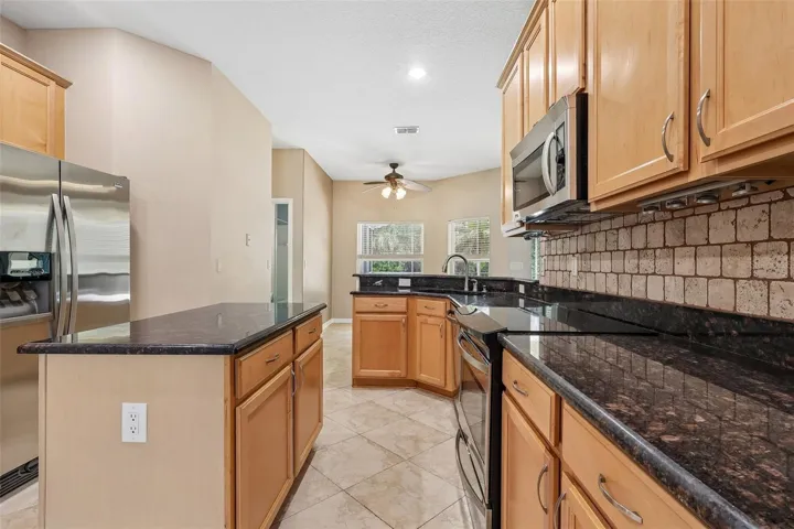 The beautifully UPDATED Kitchen is a true showpiece, featuring abundant cabinetry, granite countertops, NEW TRAVERTINE TILE BACKSPLASH, stainless steel appliances, a kitchen island, breakfast bar, closet pantry, and NEW DISPOSAL, DELTA FAUCET, and SINK DRAINS.