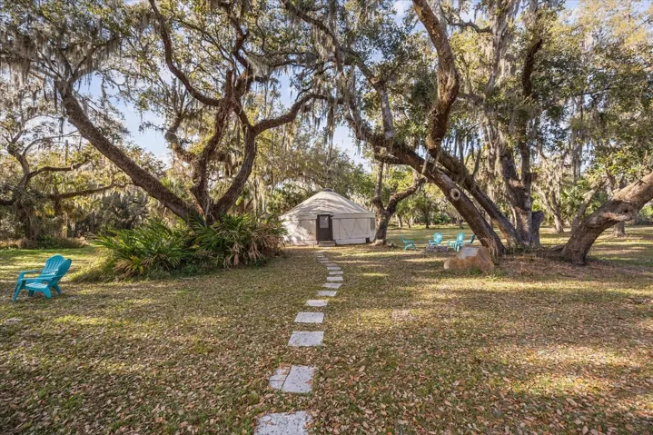 A winding stepping-stone path beneath moss-draped oaks leads to the yurt.