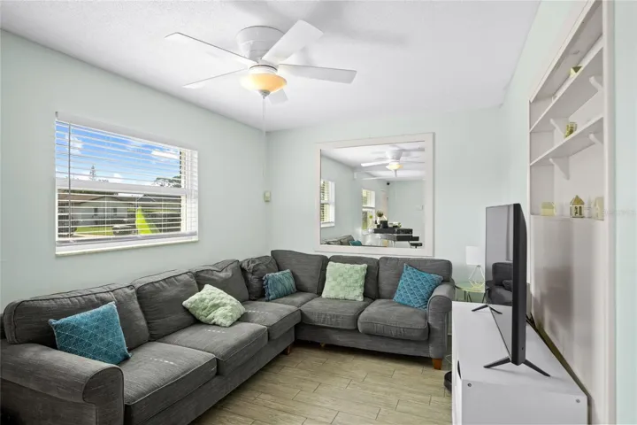A photo of the family room with a ceiling fan, built in shelving, and double pane windows.