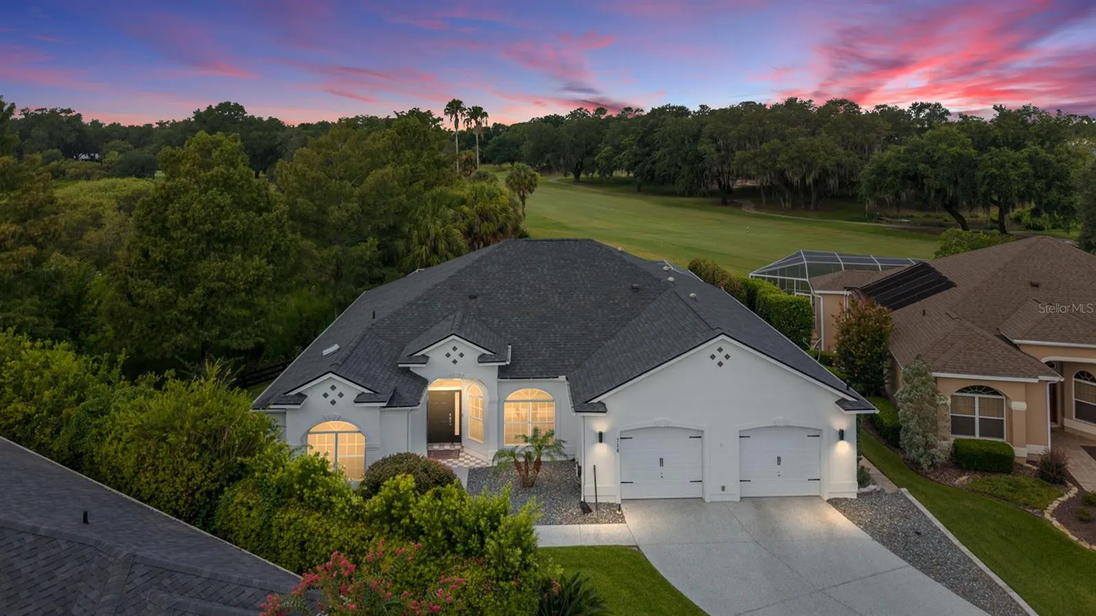 A striking sunset backdrop and warm exterior lighting create an inviting evening view of this golf course home.