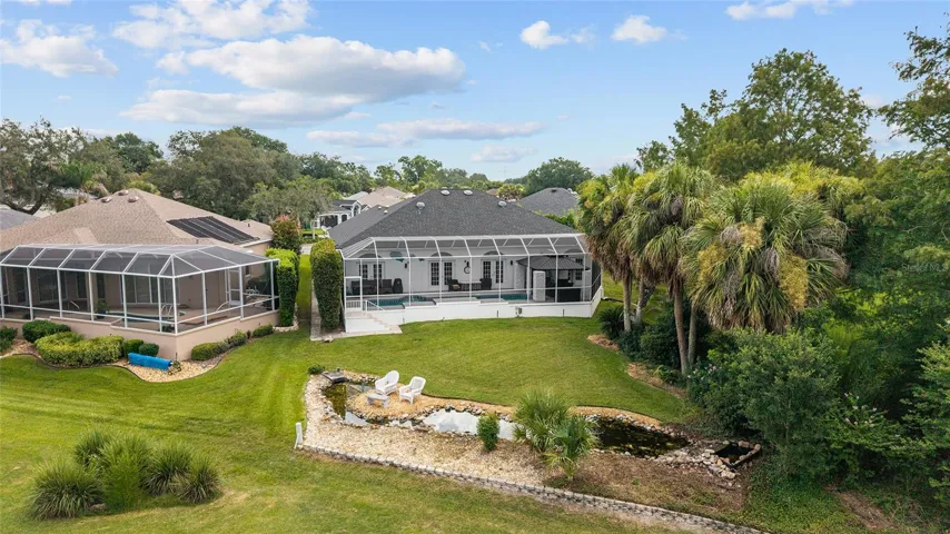 The backyard combines a screened pool enclosure, mature palms, and landscaped grounds with a picturesque golf course backdrop.