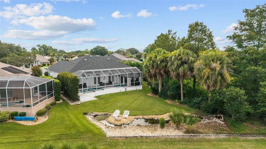 Aerial rear view highlights the home’s screened outdoor living area, lush tropical landscaping, and decorative backyard KOI POND AND WATERFALL garden feature.