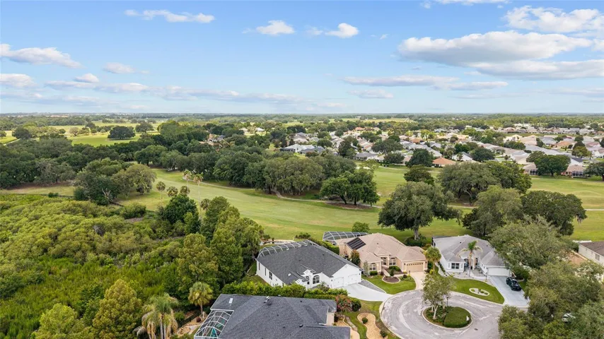 Wide aerial view illustrates the home’s peaceful cul-de-sac surroundings, mature natural landscape, and proximity to golf and water features.