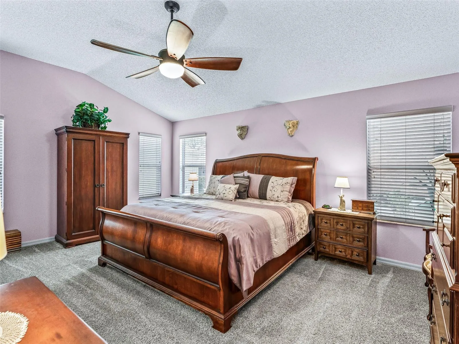 Generously sized primary suite features soft carpeting, multiple windows, a ceiling fan, and ample space for a complete bedroom furniture arrangement.