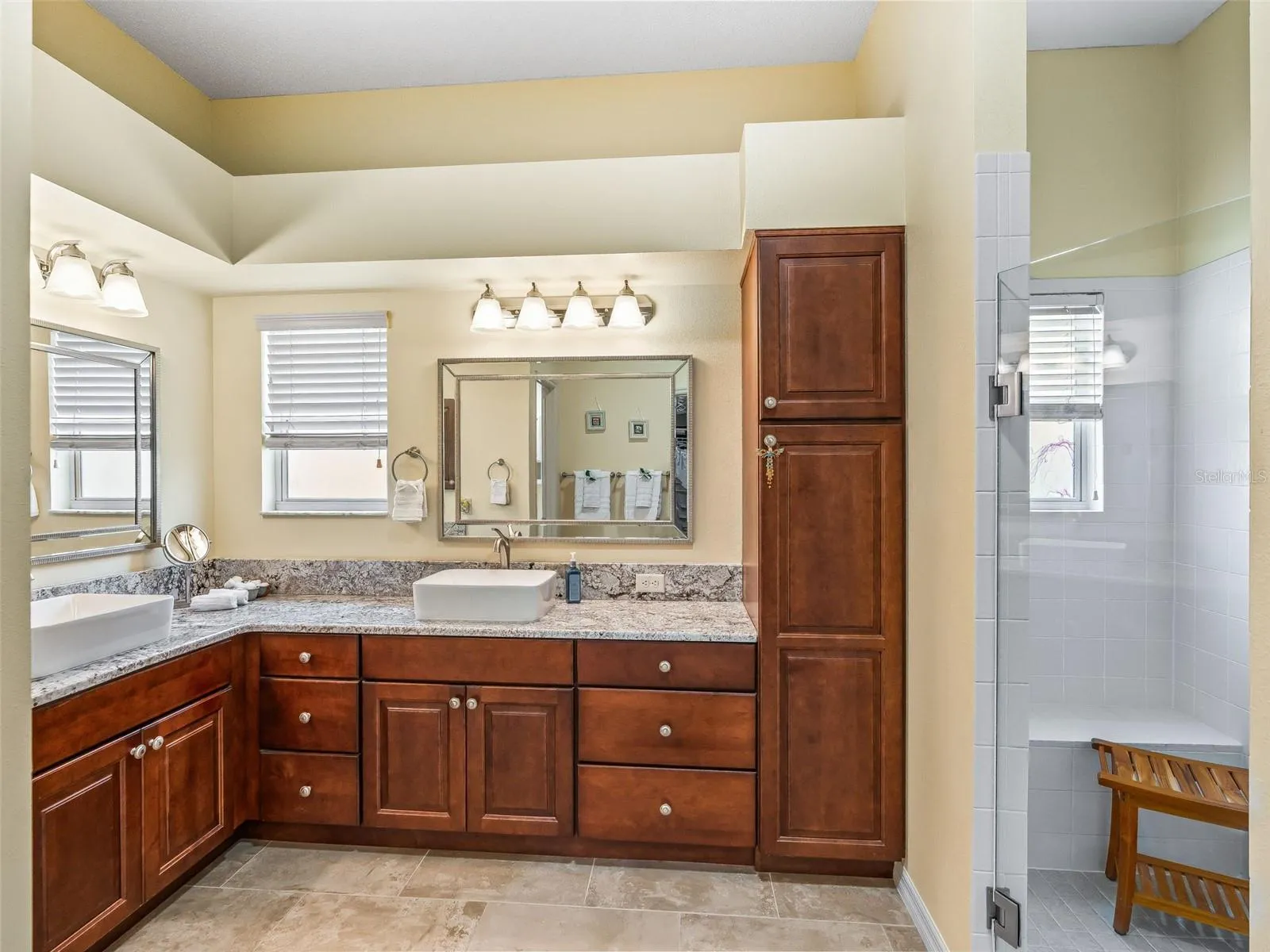 The primary bathroom offers extensive wood cabinetry, a tall linen cabinet, dual vanity areas, and multiple windows for natural light.