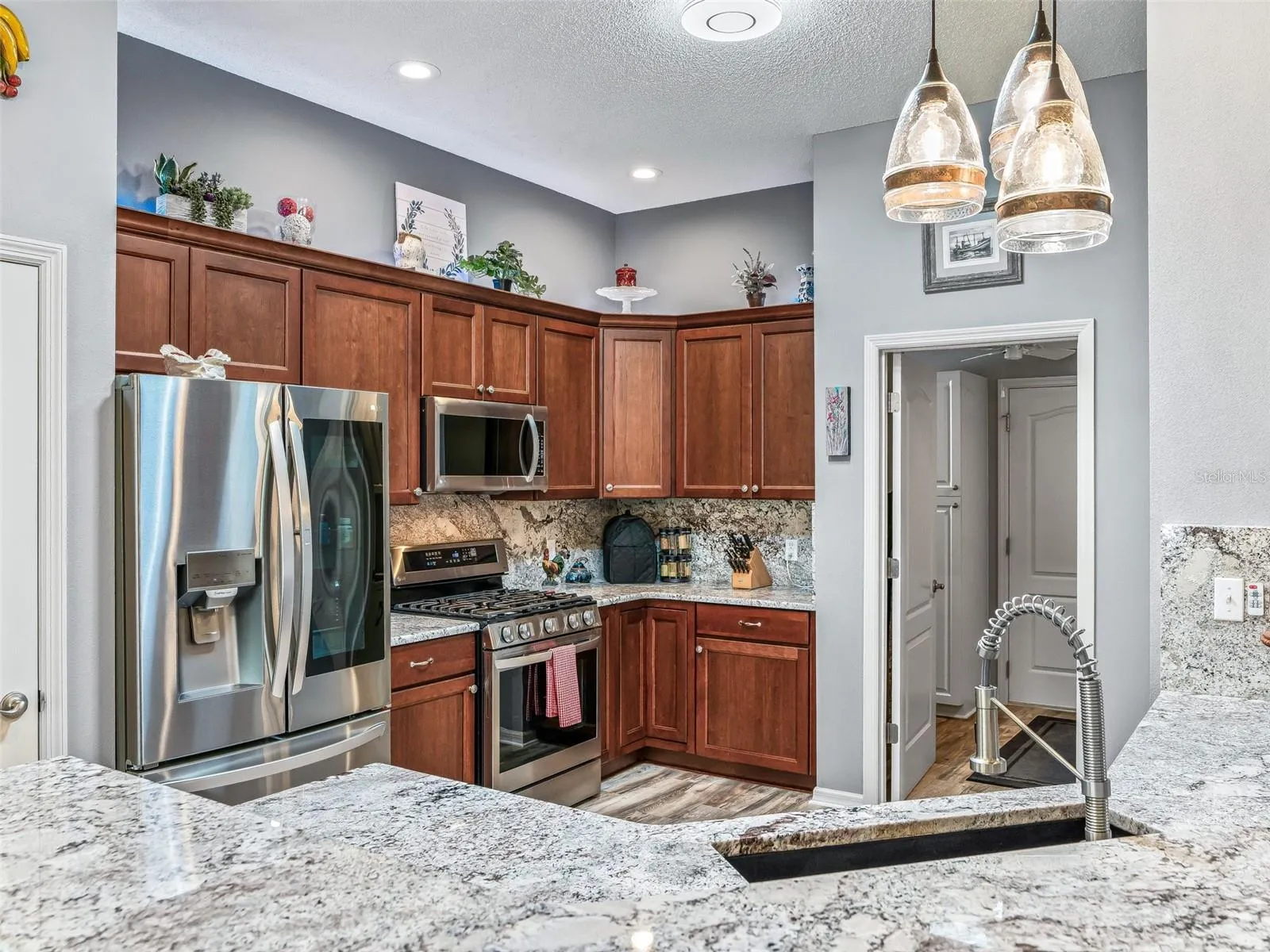 Rich wood cabinetry, granite countertops, stainless steel appliances, decorative backsplash, and pendant lighting create a polished and functional workspace.