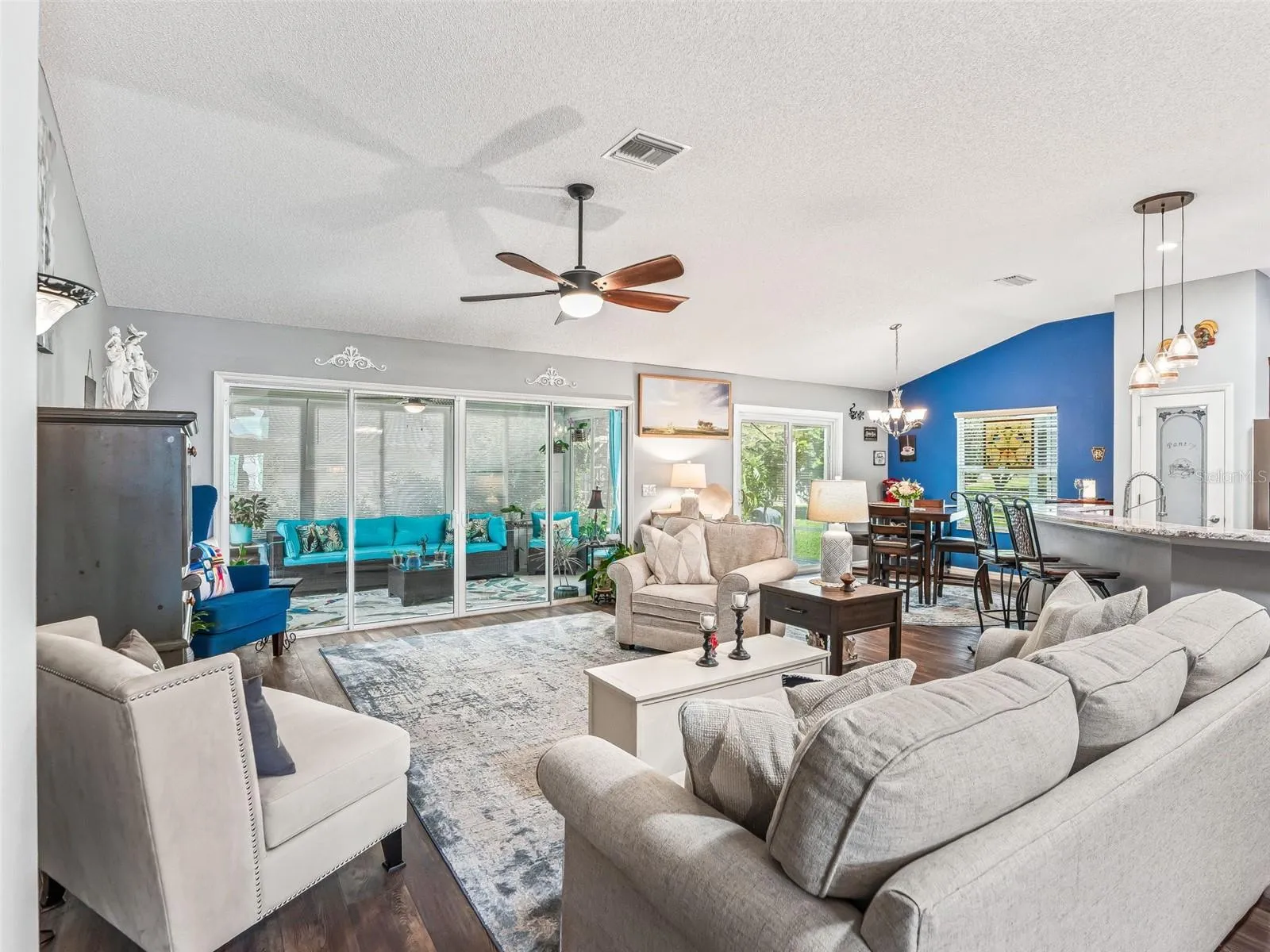 Expansive living room offers comfortable seating space, a vaulted ceiling, ceiling fan, and abundant natural light from the rear windows and glass doors.