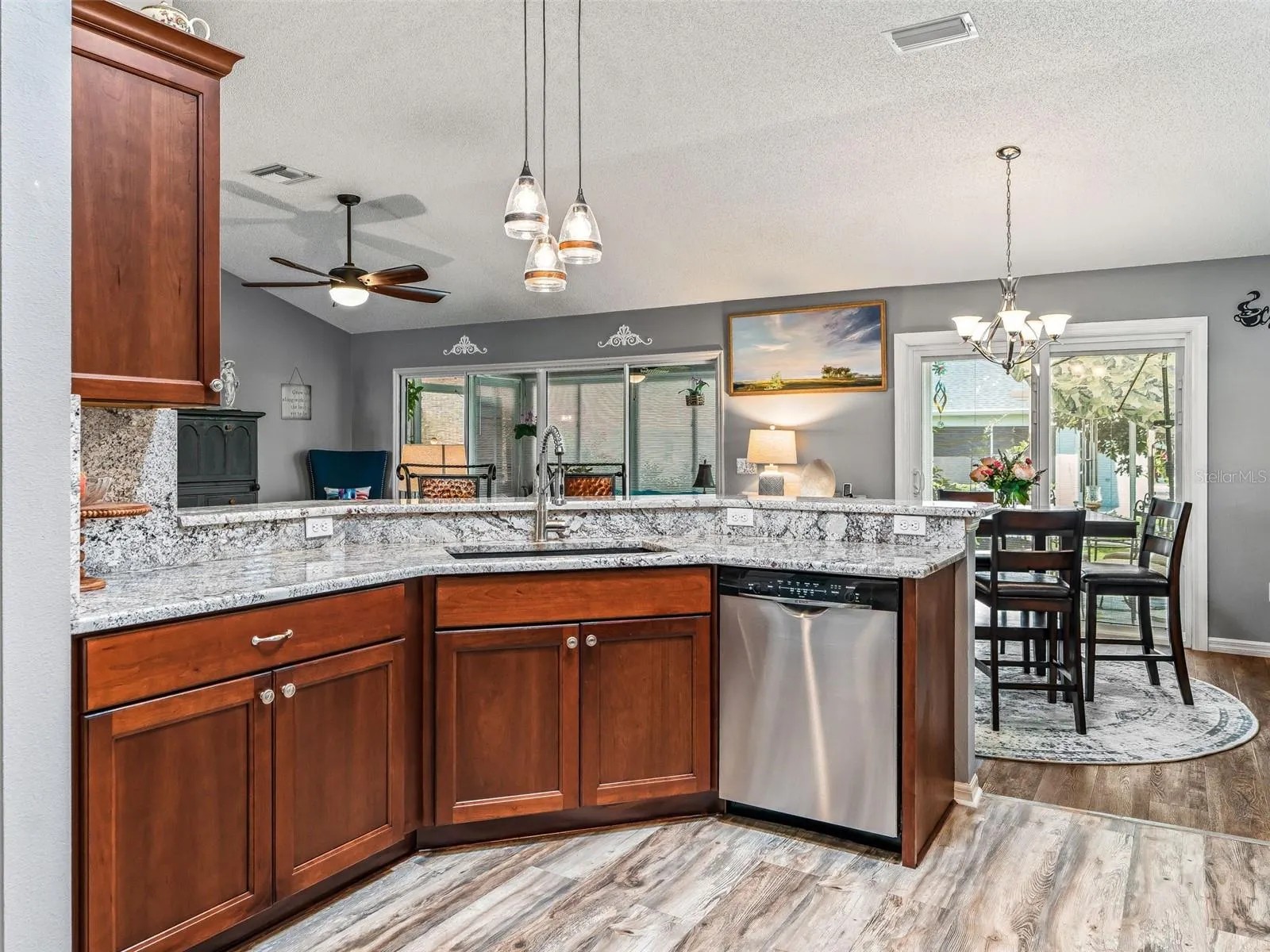 A wide granite breakfast bar with pendant lighting provides additional prep space and casual seating while maintaining an open connection to the dining and living areas.
