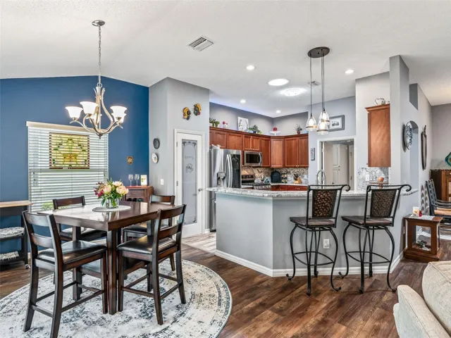 The open layout connects the dining area and kitchen, with coordinated lighting, wood-look flooring, and a breakfast bar ideal for casual seating.