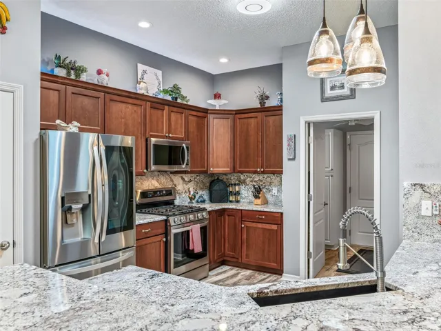 Rich wood cabinetry, granite countertops, stainless steel appliances, decorative backsplash, and pendant lighting create a polished and functional workspace.