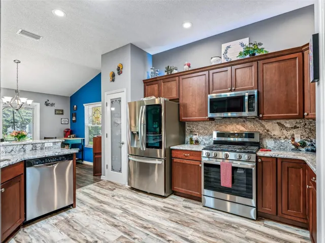 Warm wood cabinetry, stainless steel appliances, granite countertops, tile backsplash, and durable flooring combine for an attractive and practical kitchen.