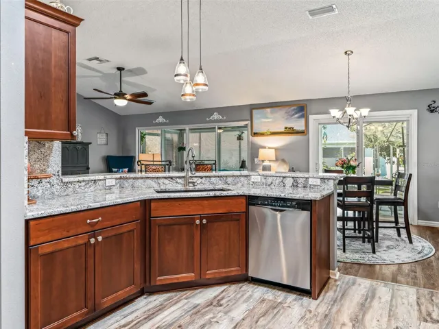 A wide granite breakfast bar with pendant lighting provides additional prep space and casual seating while maintaining an open connection to the dining and living areas.