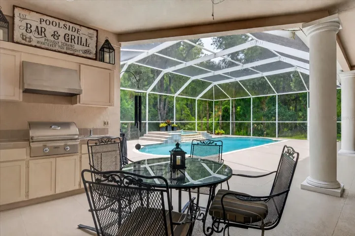 The oversized screened pool and lanai create an exceptional outdoor living space with covered seating and dining areas, an outdoor kitchenette with a stainless gas grill, and a sparkling pool paired with an elevated heated spa and cascading tiered waterfall.
